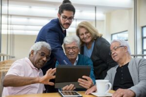 Group of seniors and a young man collaborating using a tablet during a meeting indoors.